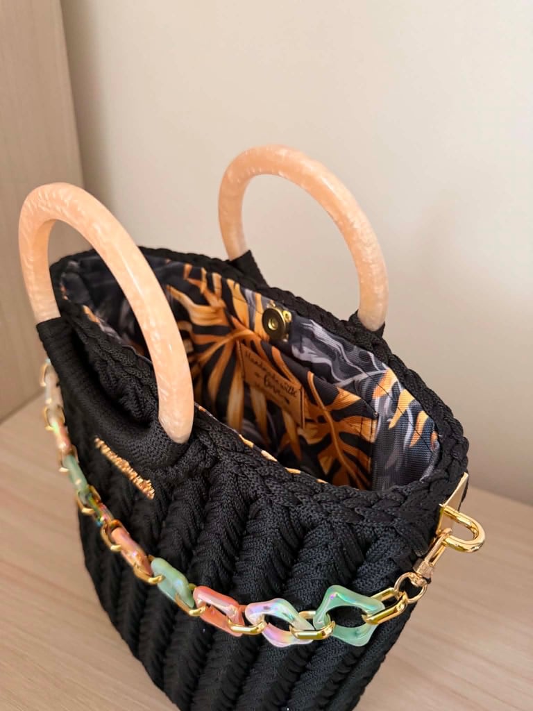 Black quilted tote bag with peach-colored handles and colorful chain detail on the front