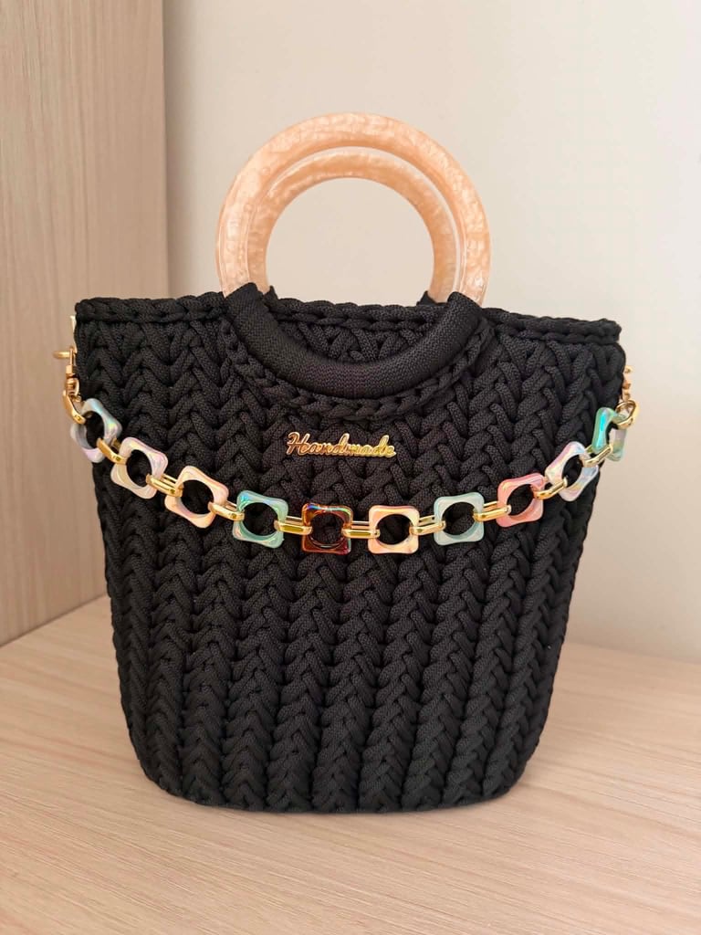Black woven tote bag with peach wooden handles and colorful chain strap detail