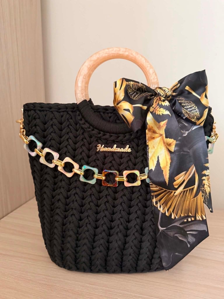 Black quilted handbag with wooden handles, gold chain strap, and decorative black and gold silk scarf bow
