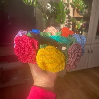 Ręka trzymająca kolorowe dziergane kule w czerwonym, żółtym, różowym, niebieskim, zielonym i brązowym